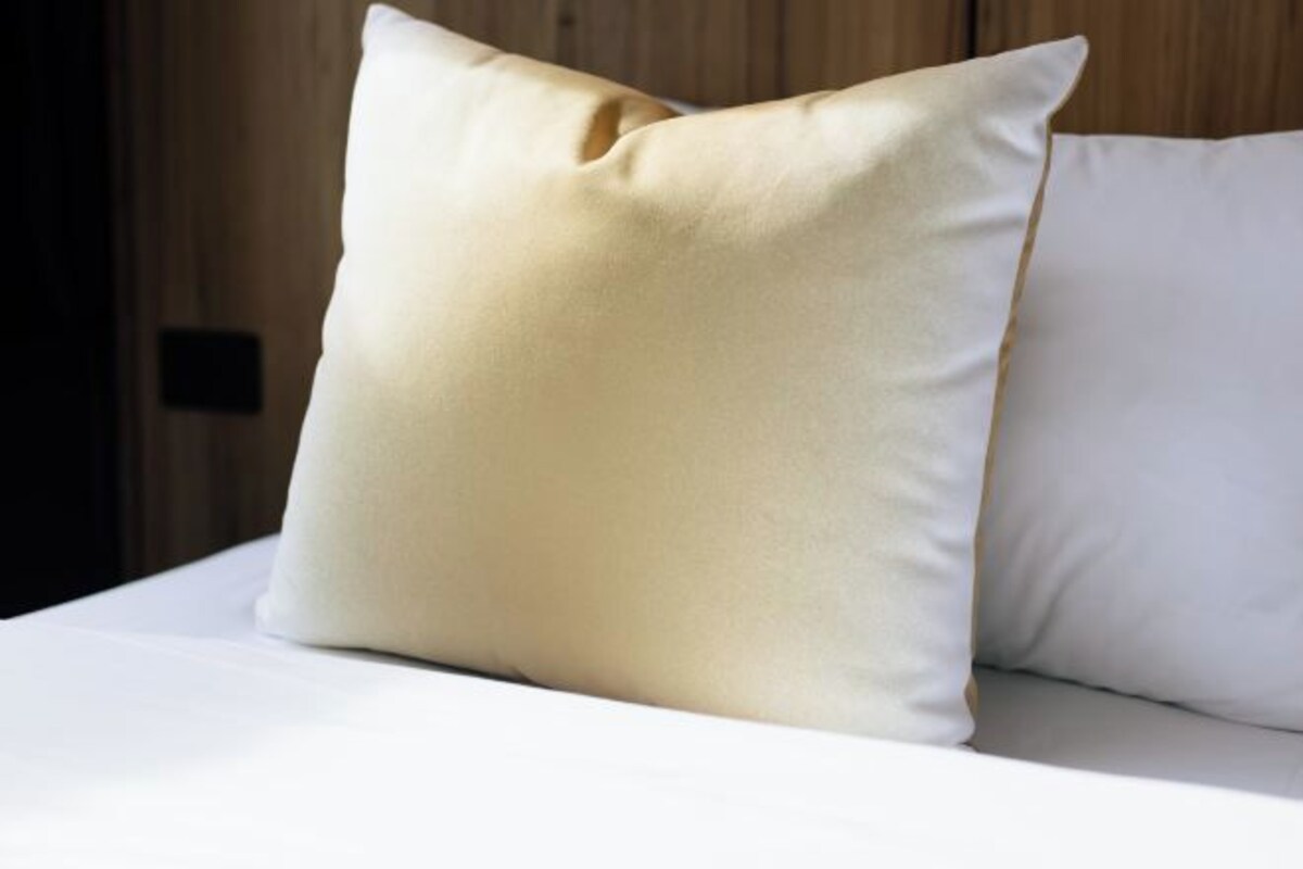 A bed with two pillows, one with a visible seam and a light color.