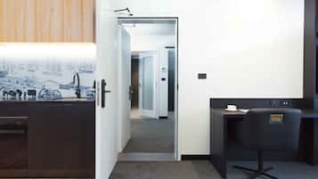 A modern hotel room with a wooden cabinet, a desk with a chair, and a view of the hallway.