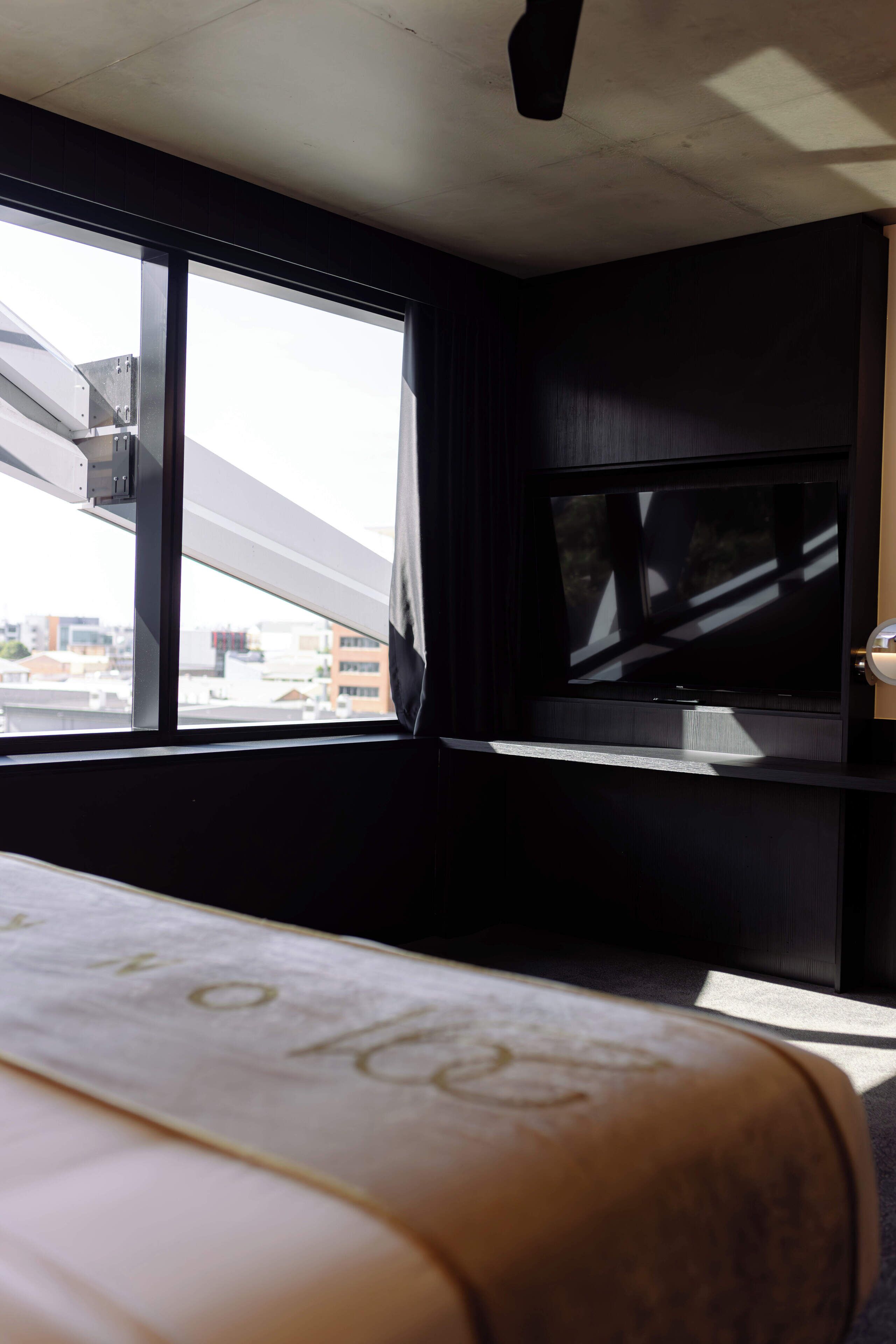 A hotel room with a bed, a television, and a window with a city view.
