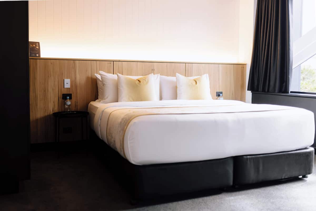 A hotel room with a large bed, a bedside table, and a window with curtains.