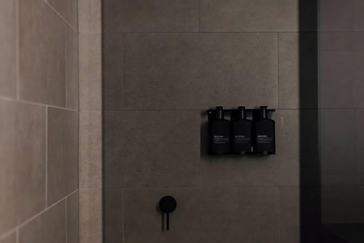 A bathroom with a tiled wall, a black towel rack, and three black bottles on the wall.