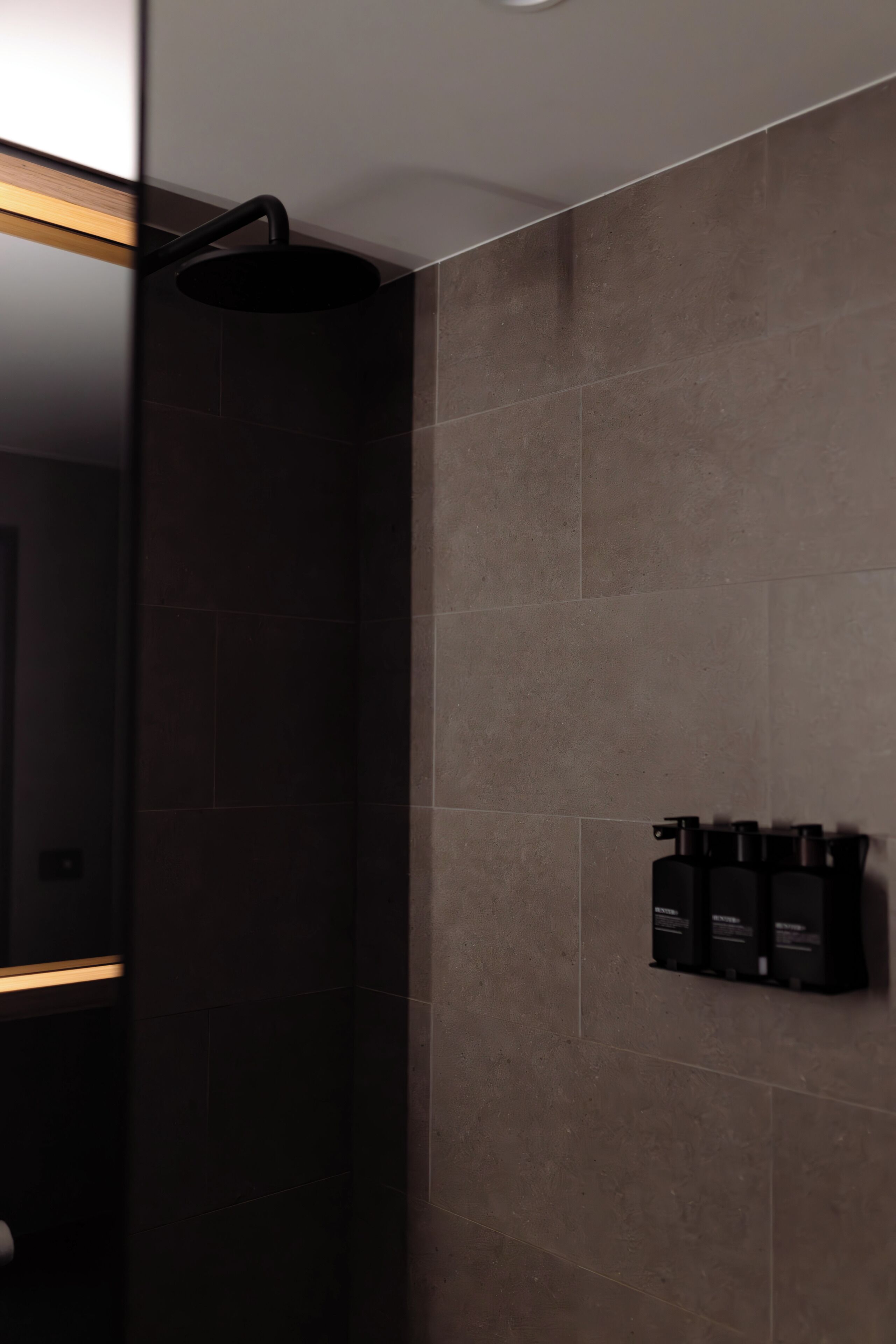 Un baño moderno con azulejos oscuros, un lavabo negro y un espejo.