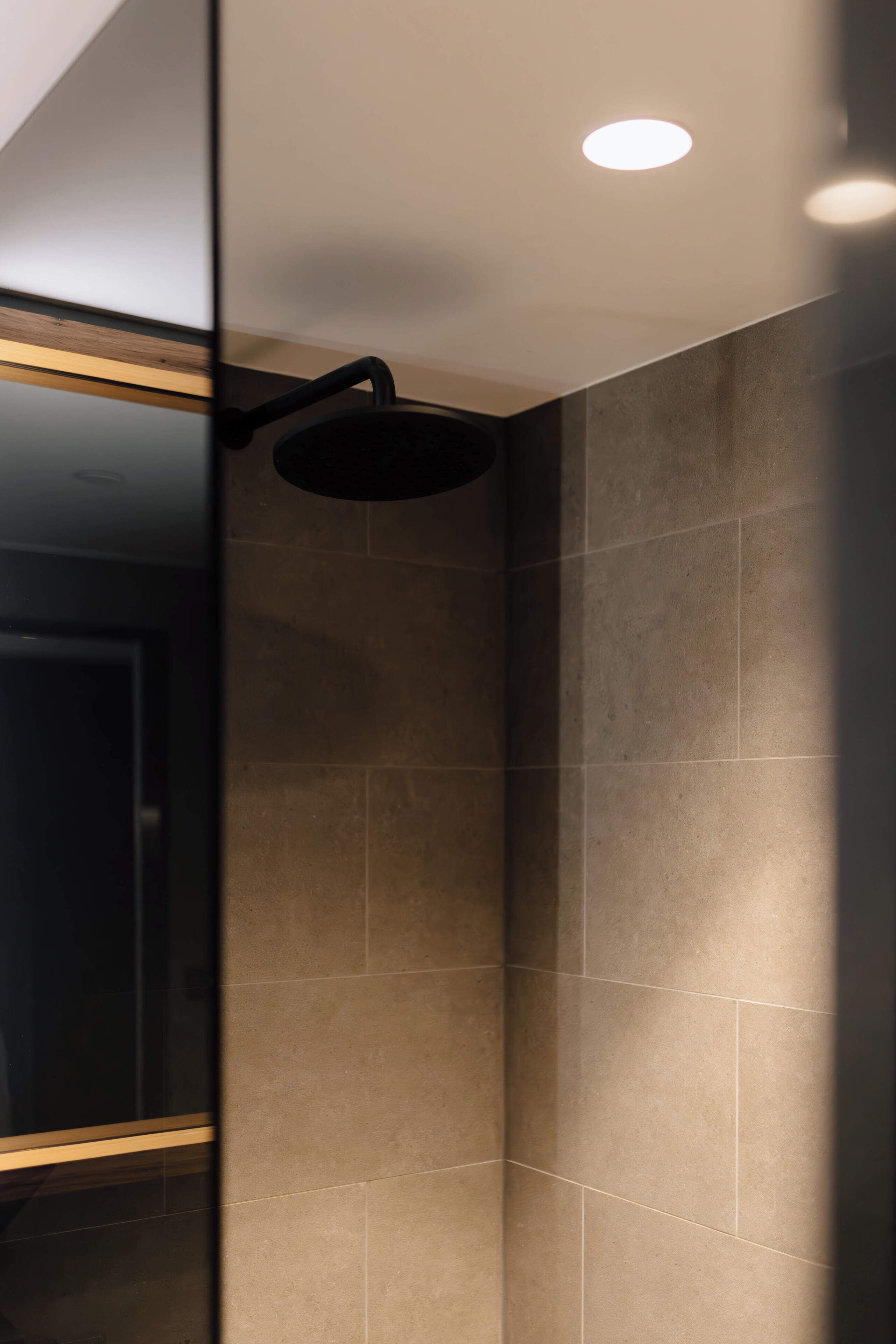 A modern bathroom with a glass shower enclosure, recessed ceiling lighting, and tiled walls.
