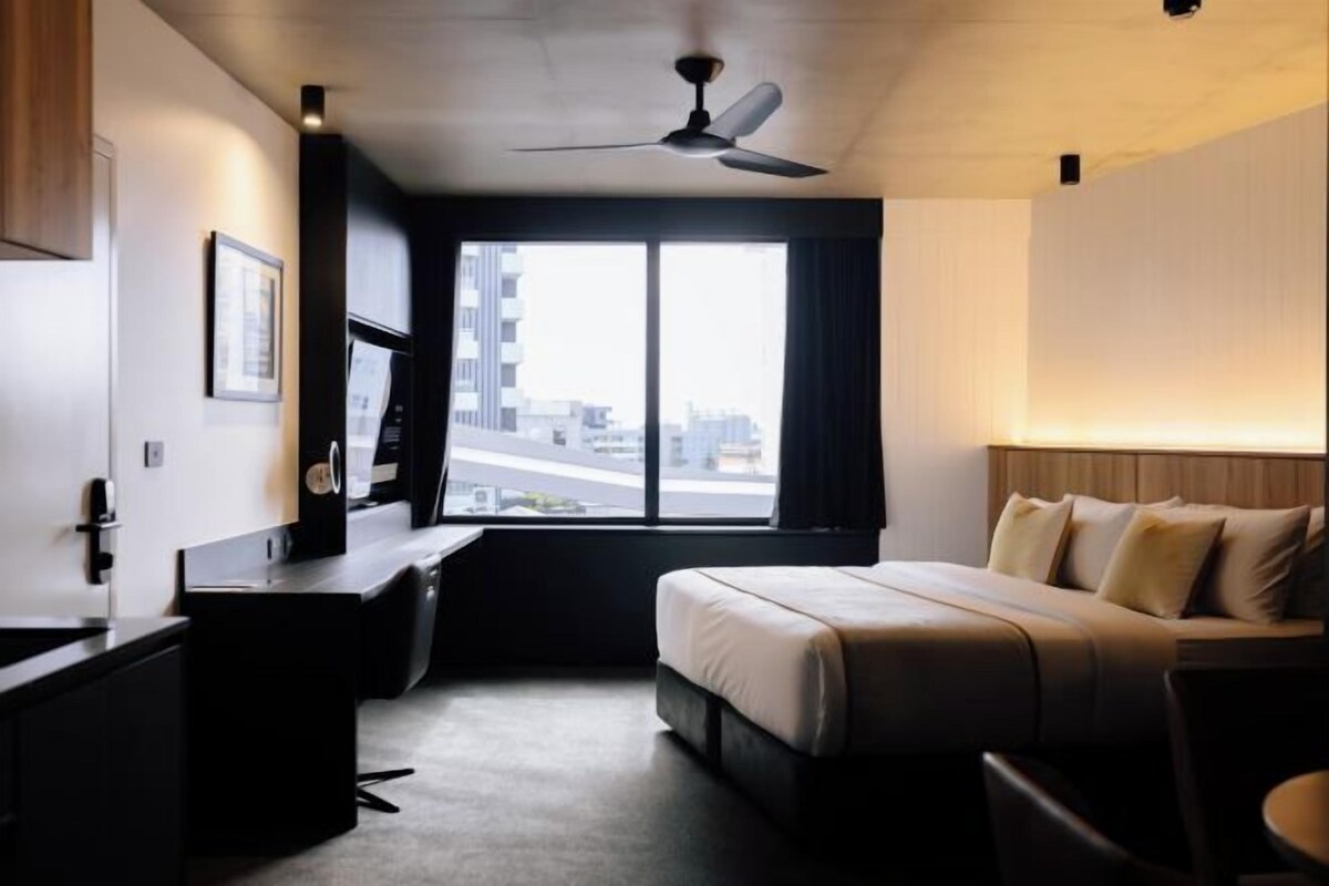 A hotel room with a bed, desk, and a large window offering a city view.