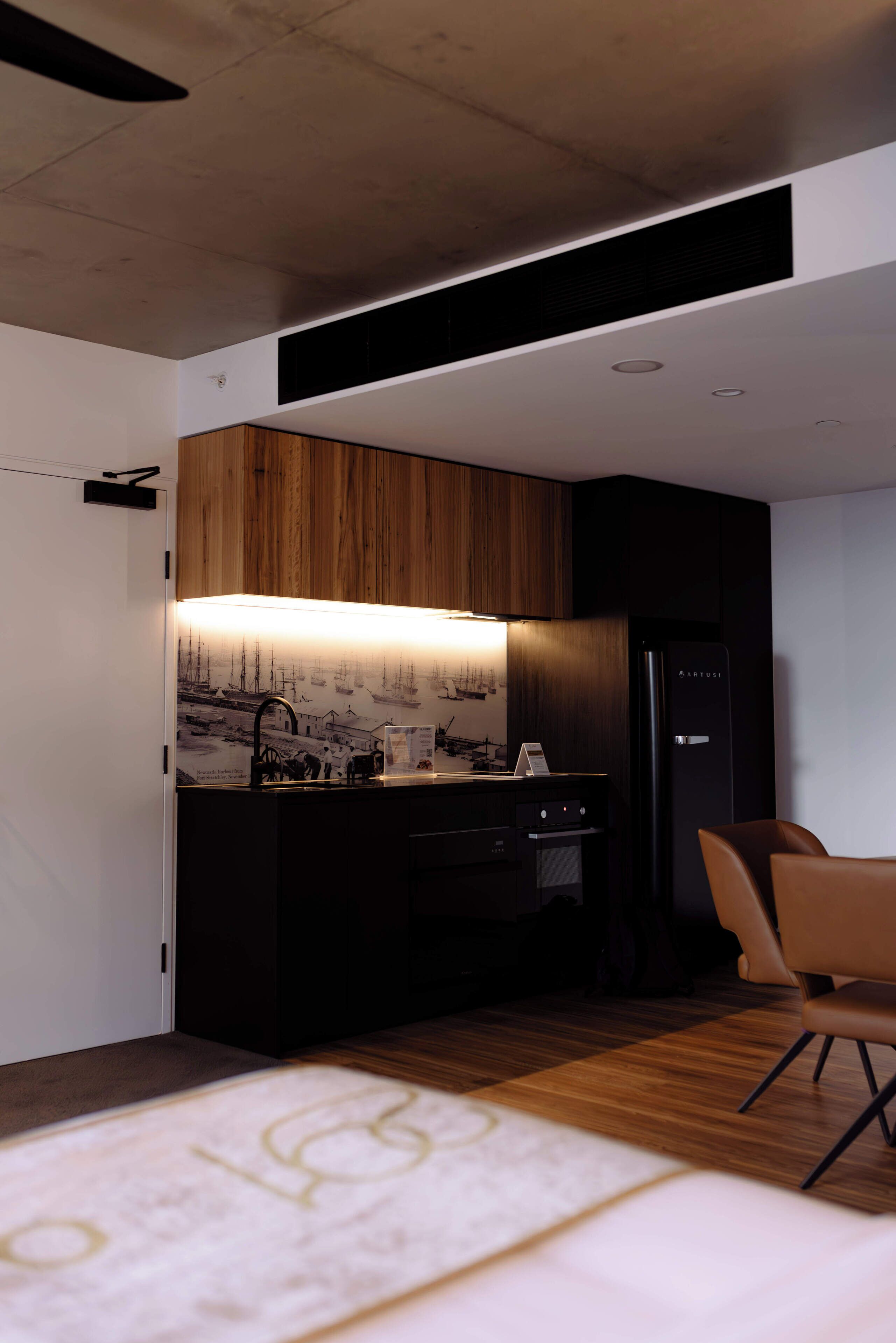 A modern kitchen with wooden cabinets, a black refrigerator, and a dining area with a chair.