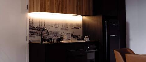 A modern kitchen with wooden cabinets, a black refrigerator, and a dining area with a chair.