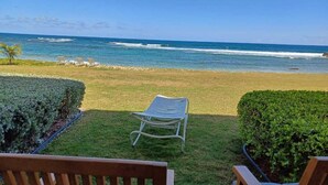 Une vue d’une plage avec une zone herbeuse, une chaise en métal et un banc en bois.