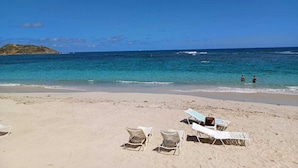 Une plage avec des chaises longues blanches et un ciel d’un bleu limpide.