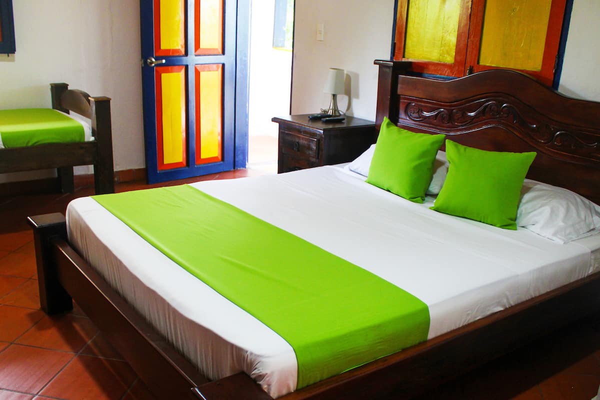 A neatly made bed with a green bedspread and pillows, a wooden headboard, and a nightstand with a lamp.