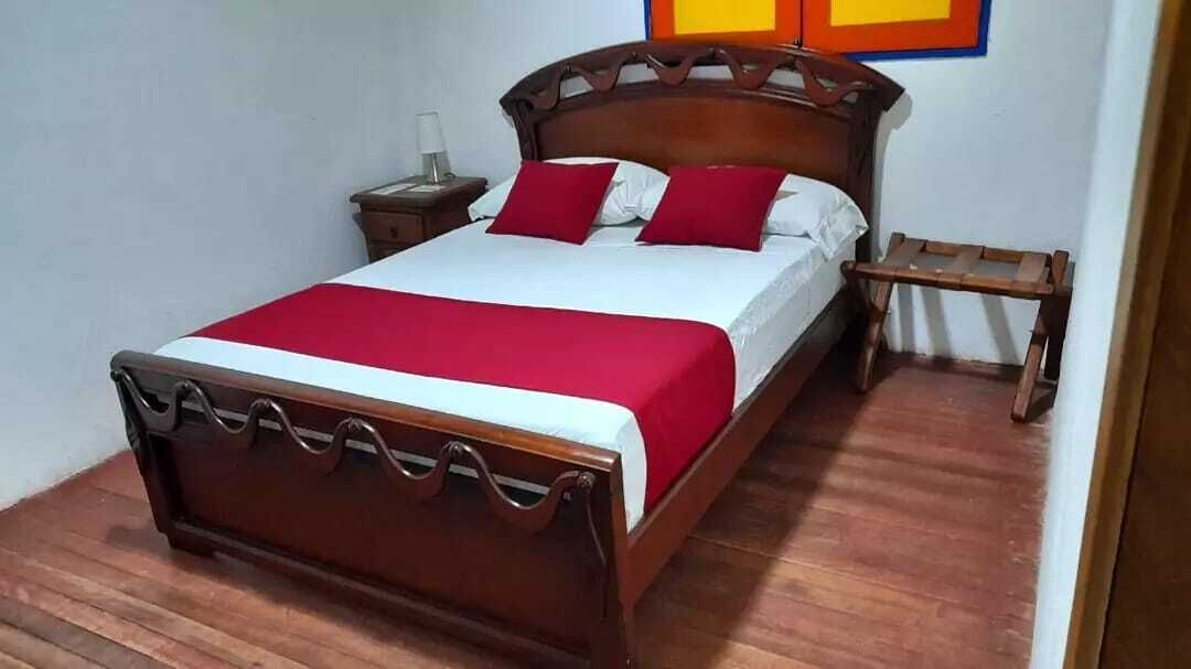 A neatly made bed with a wooden frame, white bedding, and red pillows.