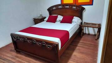 A neatly made bed with a wooden frame, white bedding, and red pillows.