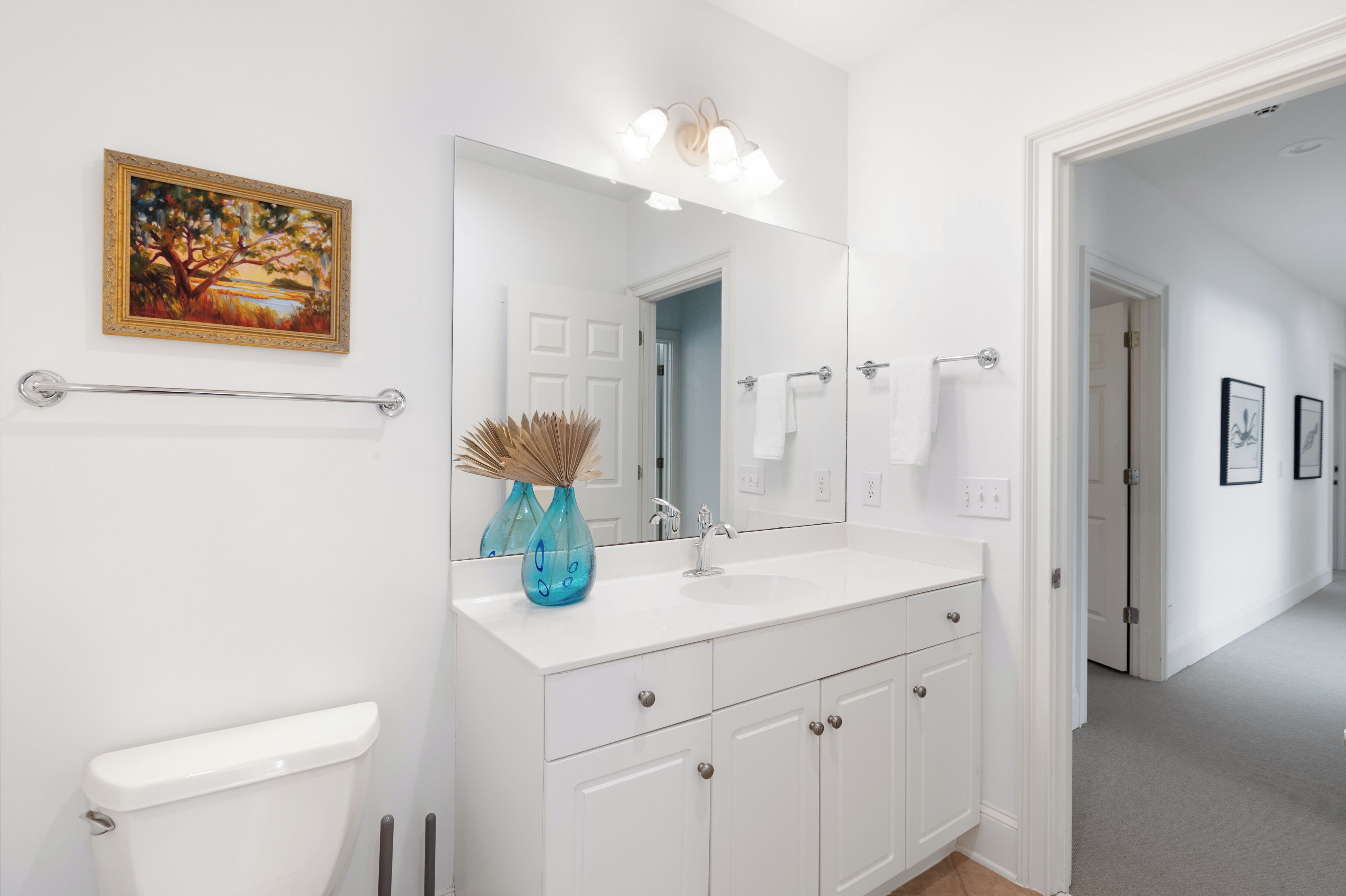 A modern bathroom with a white vanity, a large mirror, and a painting of a tree.