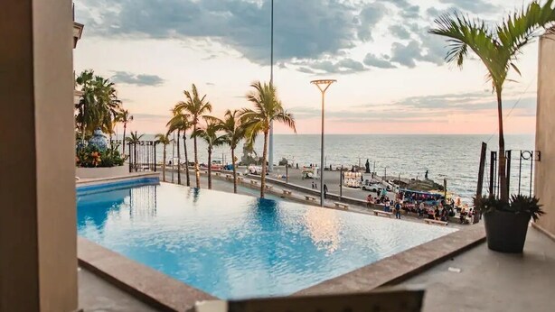 A pool area with a view of the sea, palm trees, and a street with people. - Condos Clauss (Mazatlán)