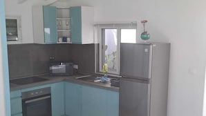 A compact kitchen with teal cabinets, a stainless steel refrigerator, a microwave, and a stove. - Tropical Studio (Collectivité de Saint-Martin)