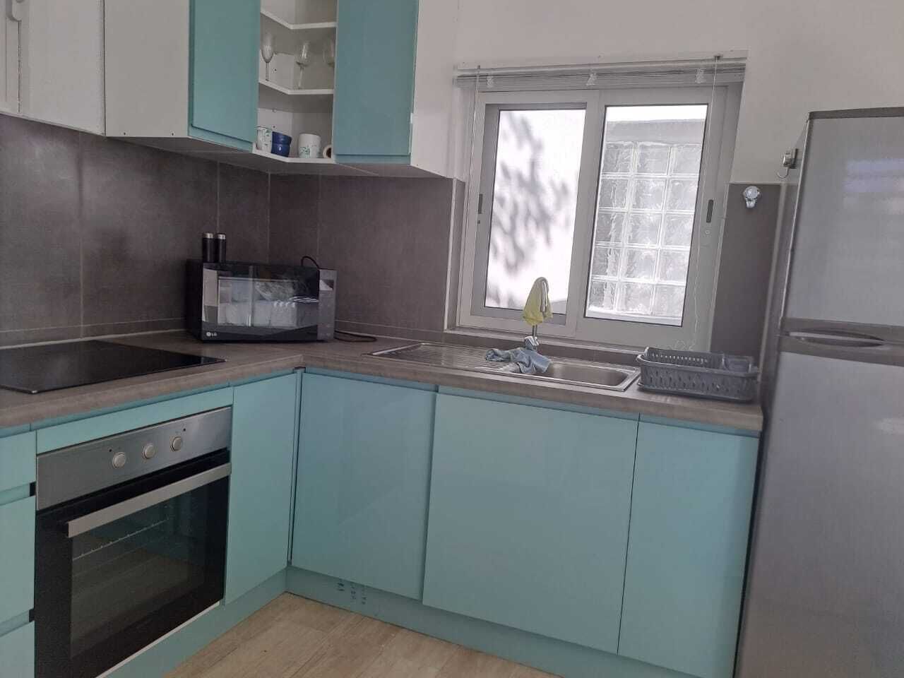 A kitchen with teal cabinets, a black stove, and a window with a view.