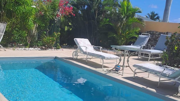 A rectangular swimming pool with clear blue water, surrounded by white lounge chairs and a small table. - Tropical Studio (Collectivité de Saint-Martin)