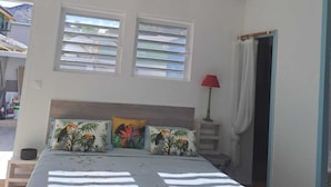 A bedroom with a bed, two windows, a nightstand, and a red lamp. - Tropical Studio (Collectivité de Saint-Martin)