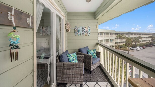 A balcony with wicker furniture, a ceiling fan, and a view of a parking lot and buildings. - Perfect Oceanfront Condo w/Stunning Ocean View! Community Pool, Fishing Pier! (Isle Of Palms)