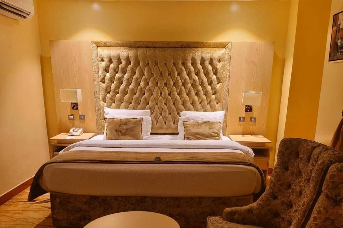 A hotel room with a large bed, two bedside tables, a round table, and two armchairs.