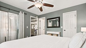 Un dormitorio con cama, ventilador de techo, espejo y puerta.