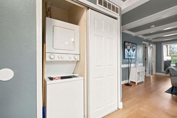 A laundry room with a washer and dryer, a door leading to a hallway, and a window with blinds.