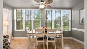 A dining area with a table, chairs, a ceiling fan, and large windows with blinds. - Walk-in Golf Course View Condo with Lock-off Double Suite (Branson)