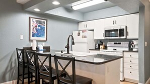 A compact kitchen with white cabinets, a microwave, a refrigerator, and a dining area with four chairs. - Walk-in Golf Course View Condo with Lock-off Double Suite (Branson)
