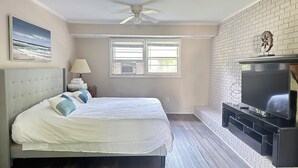 Een slaapkamer met een bed, een plafondventilator, een televisie en een bakstenen muur.