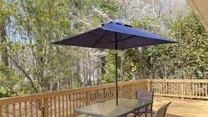 Een glazen tafel met stoelen en een blauwe parasol op een houten terras.