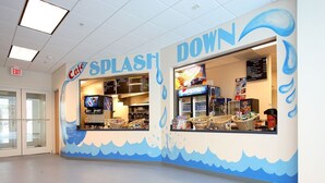 Een café genaamd 'Cafe Splash Down' met een muurdecoratie in golfmotief, een menubord en een koelkast vol drankjes.