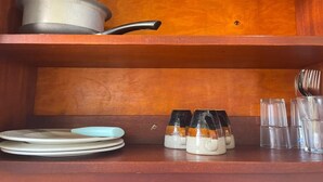 En træhylde med en metal gryde, to tallerkener, to krus og flere glas.