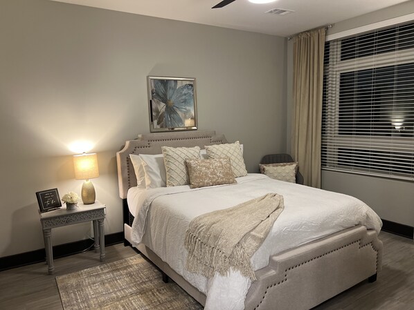 Una camera da letto con un letto grande, un comodino con una lampada, un quadro incorniciato e una finestra con tende.