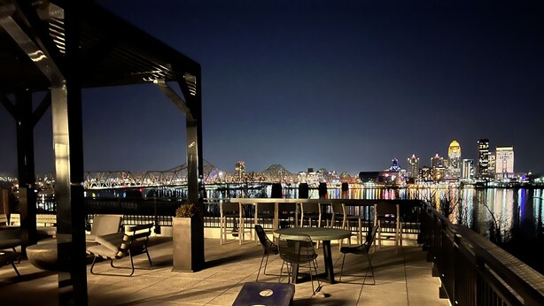 Een terras met tafels en stoelen, een overdeeld gedeelte en uitzicht op een stadshemelbeeld over het water.
