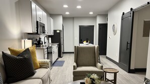 Een moderne woonkamer met een bank, fauteuil, salontafel en een keuken op de achtergrond.