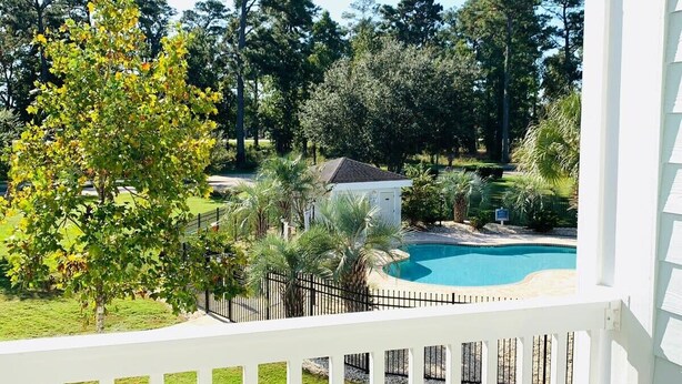 Un balcon doté d’une table et de chaises en verre, offrant une vue sur une piscine et une végétation luxuriante.