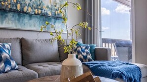 A modern living room with a gray sofa, a blue and white patterned throw blanket, and a vase with green branches.