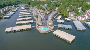 An aerial view of a waterfront property with multiple buildings, a central swimming pool, and a road connecting the structures.
