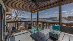 A covered outdoor deck with a view of a body of water, a grill, and seating.