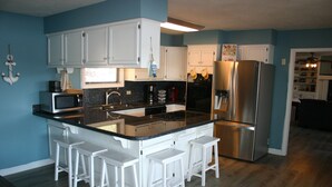 Una cocina moderna con armarios blancos, un refrigerador de acero inoxidable y una isla central con taburetes de bar.