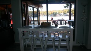 Un área de comedor con una mesa y sillas, un pastel en la mesa, y vistas a un lago con barcos.