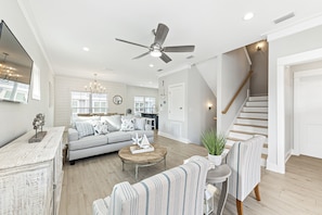 A spacious living room with a gray sofa, striped armchairs, a wooden coffee table, and a ceiling fan. A staircase with wooden steps leads to an upper level. - Summer Salt Escape | Zero Entry Pool | Lake for Fishing | My Beach Getaways (Orange Beach)