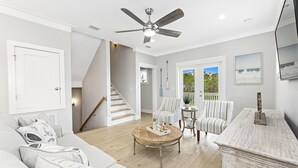 Ein geräumiges Wohnzimmer mit Deckenventilator, einer Treppe, einem großen Fenster mit Ausblick und einer gemütlichen Sitzecke mit Couchtisch.