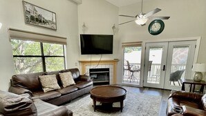 A spacious living room with a large brown leather sofa, a round coffee table, and a flat-screen TV mounted above a fireplace. - Lissa's Retreat- 4 BDRM 3 BA Sleeps 12! Indoor Pool, Gym, Fishing, Golf, & Park (Branson)