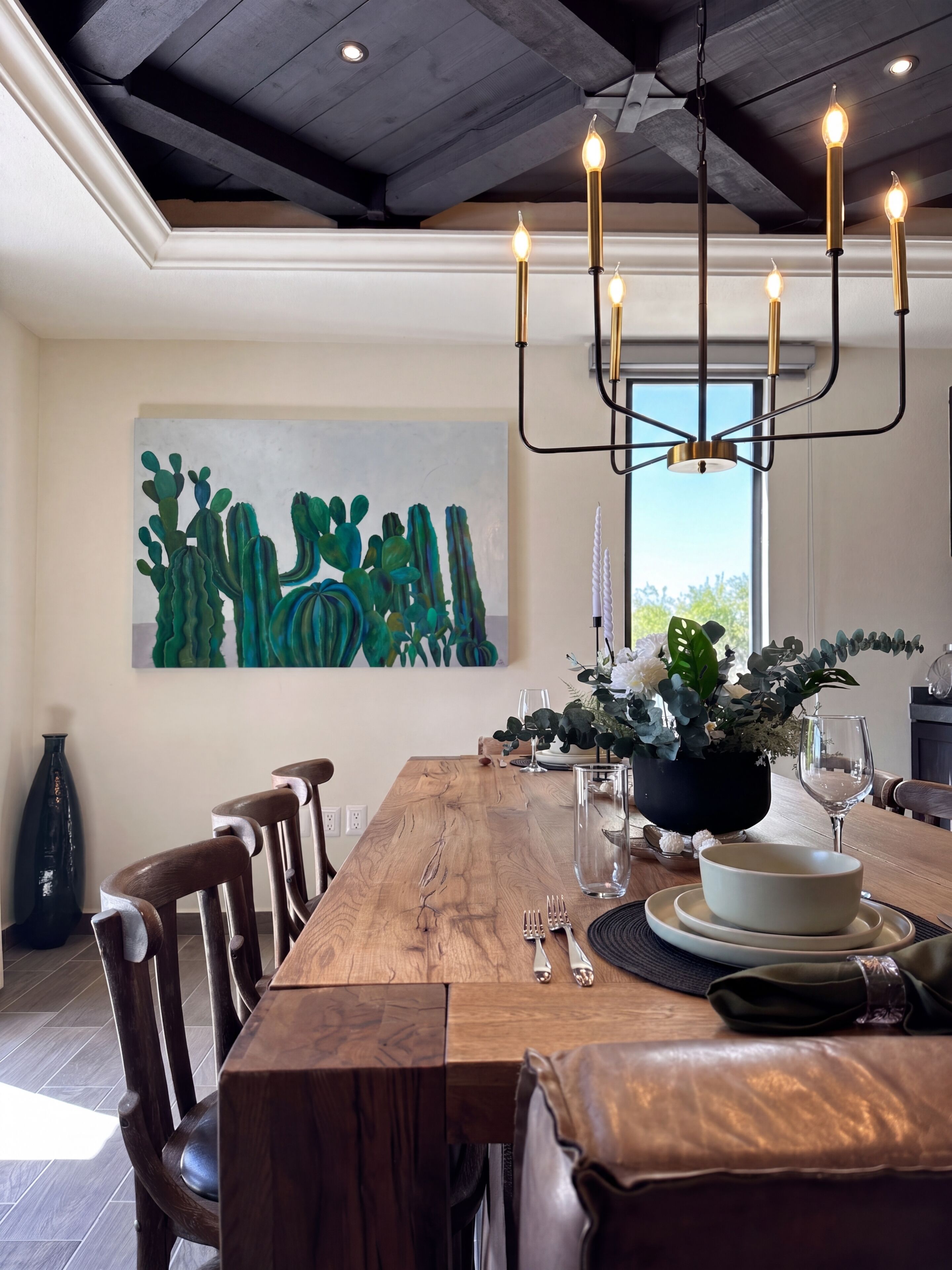 A dining area with a wooden table set for four, a chandelier, and a large abstract painting on the wall.