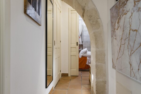 A hallway with a tiled floor, a door leading to a room with a bed, and a marble-patterned wall.