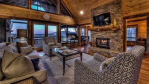 A cozy cabin interior with a stone fireplace, leather sofas, and a large window overlooking a scenic landscape. - The Silver Fox - Modern Chic Decor | Hot Tub | Aska Adventure Area (Blue Ridge)