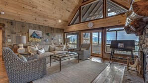 A cozy living room with a wooden ceiling, large windows, and a stone wall. - The Silver Fox - Modern Chic Decor | Hot Tub | Aska Adventure Area (Blue Ridge)