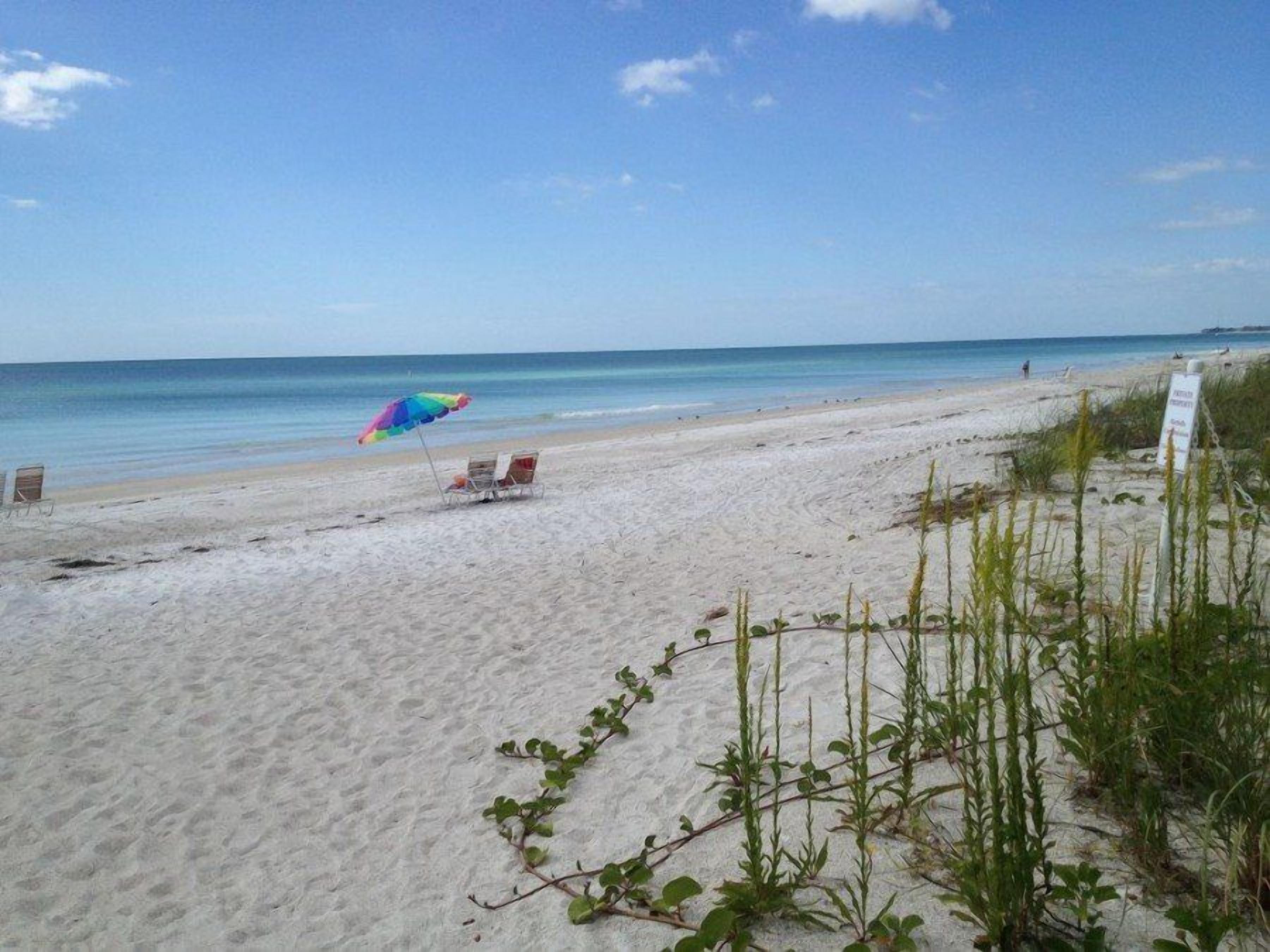 A beach with a clear sky, a colorful umbrella, and a sign indicating a beach area.