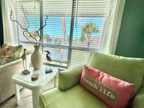 A room with a green sofa, a small white table, and a window with blinds.