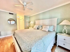 Une chambre à coucher avec un lit, des tables de chevet, un ventilateur de plafond et un miroir.